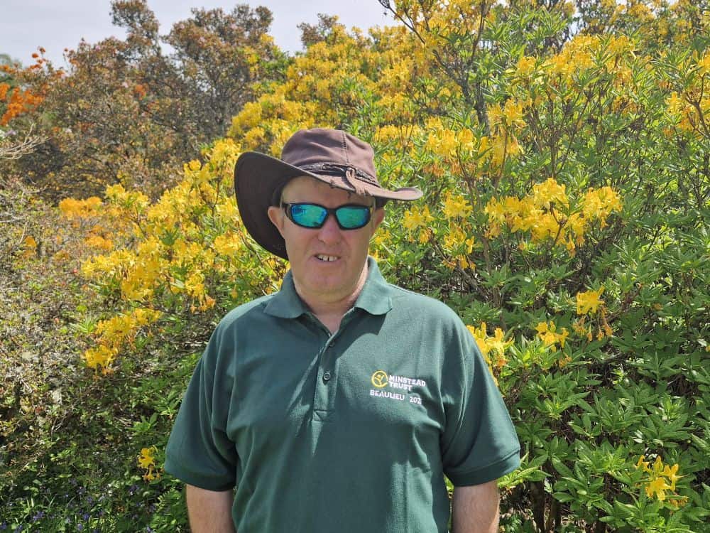 Robert in front of yellow azalea (1) Young man in green top standing in front of hatched structure at Furzey Gardens.