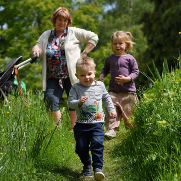 Little boy running in the garden with gran and little girl in the background